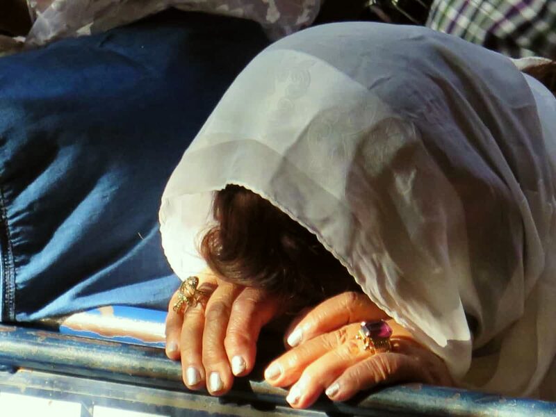 A pilgrim's hands laid flat on the Stone of Anointing, head bowed under a veil.
