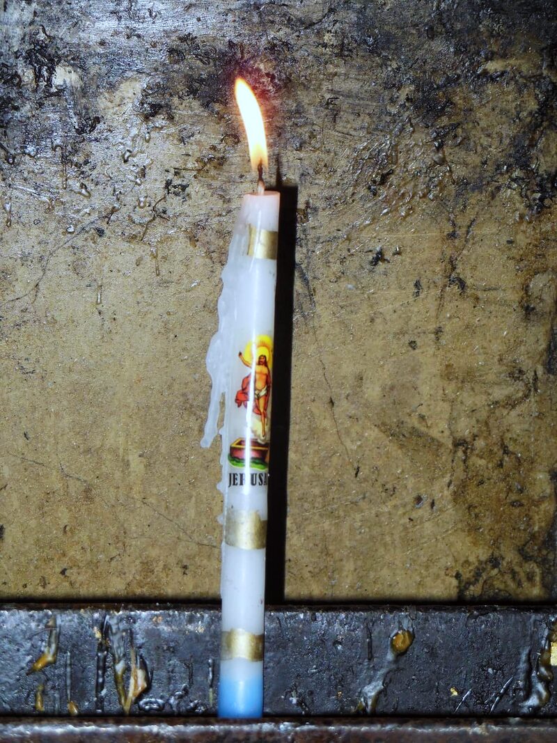 A candle burning against the wax-scarred marble of the Aedicule, the Tomb of Jesus.