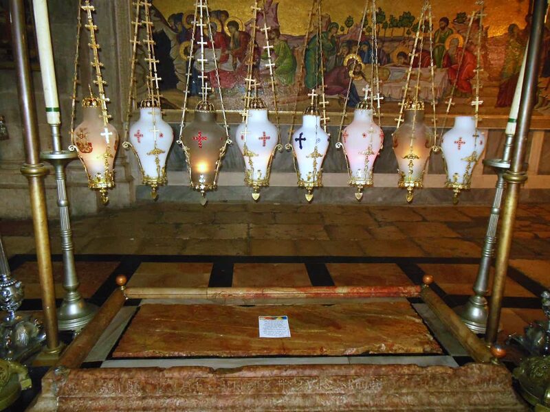 A printed prayer card resting on the Stone of Anointing, under the rank of hanging lamps.